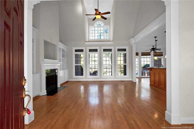 unfurnished living room featuring a fireplace with flush hearth, a ceiling fan, wood finished floors, a high ceiling, and decorative columns