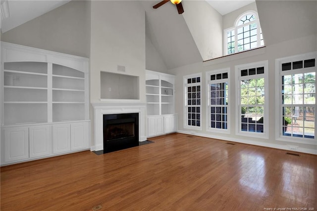 unfurnished living room with a wealth of natural light, a fireplace with flush hearth, ceiling fan, and wood finished floors