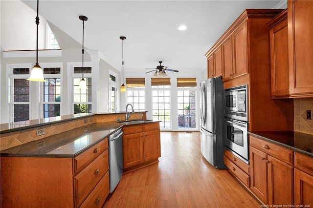 kitchen with backsplash, brown cabinets, stainless steel appliances, a ceiling fan, and a sink