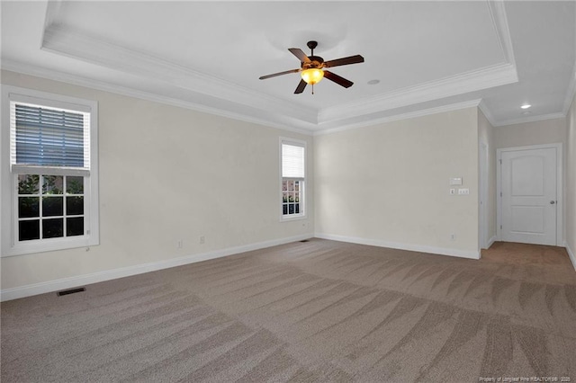 carpeted empty room featuring visible vents, baseboards, a tray ceiling, ornamental molding, and a ceiling fan