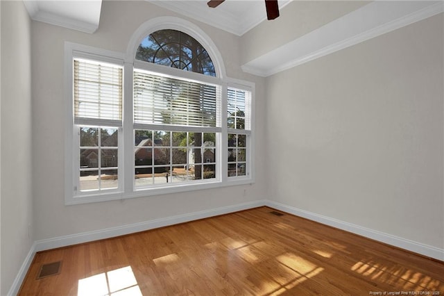 spare room featuring visible vents, crown molding, baseboards, wood finished floors, and a ceiling fan