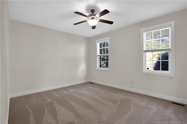 carpeted spare room with plenty of natural light, visible vents, a ceiling fan, and baseboards