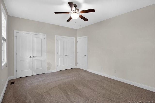 unfurnished bedroom with visible vents, baseboards, carpet, and multiple closets