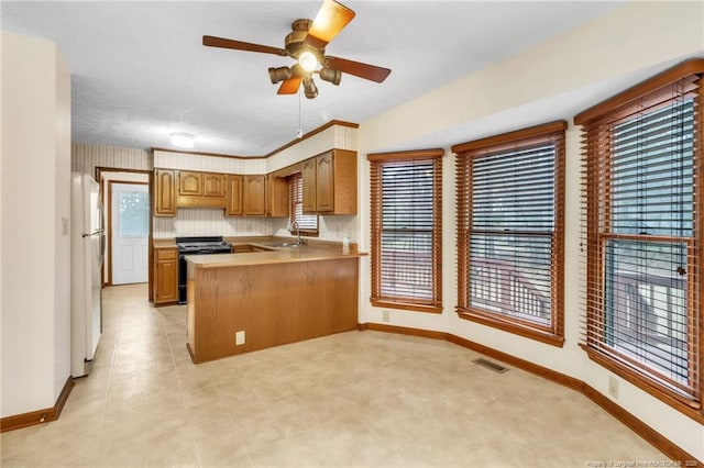 kitchen featuring visible vents, black gas range, a peninsula, freestanding refrigerator, and a sink