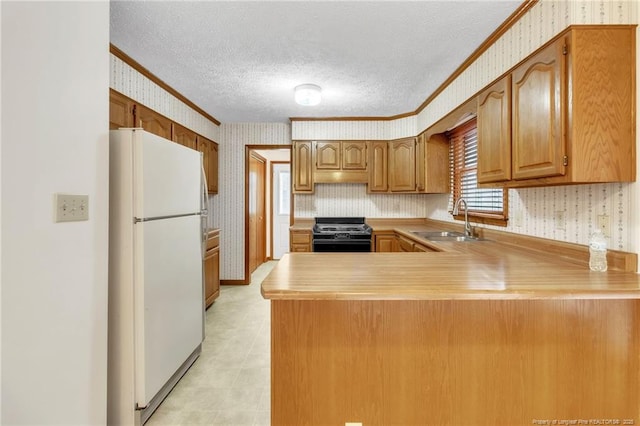 kitchen featuring a sink, freestanding refrigerator, gas stove, a peninsula, and wallpapered walls