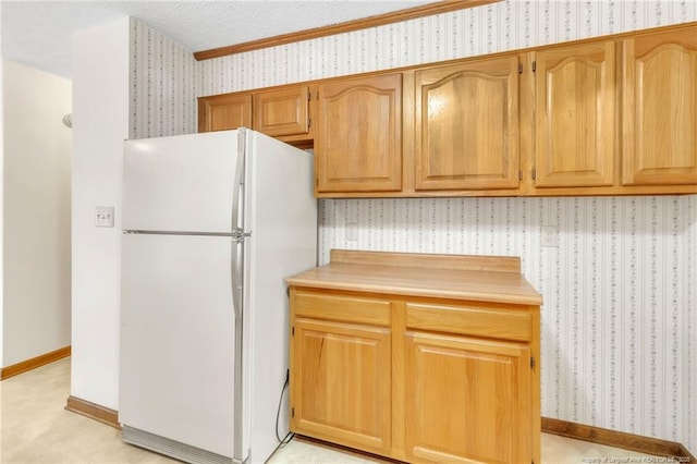 kitchen featuring wallpapered walls, freestanding refrigerator, baseboards, and light countertops