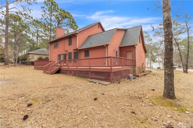 back of house with a wooden deck, a chimney, and roof with shingles