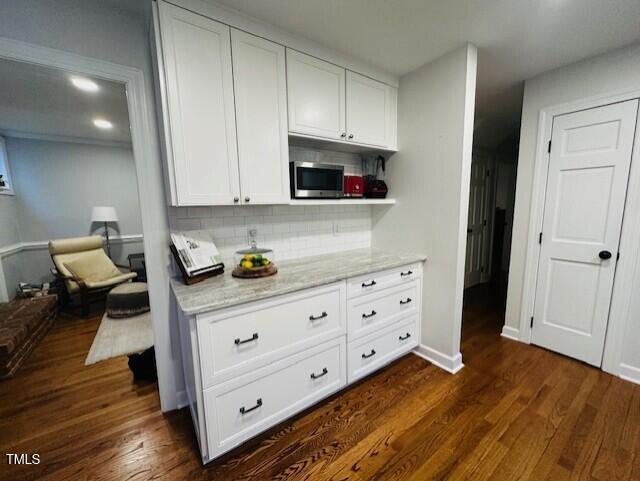 kitchen featuring stainless steel microwave, backsplash, white cabinets, and dark wood-style flooring