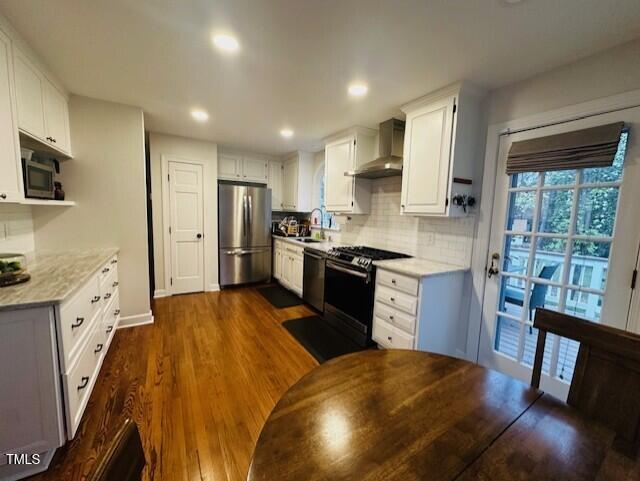 kitchen with a sink, backsplash, dark wood finished floors, stainless steel appliances, and wall chimney range hood