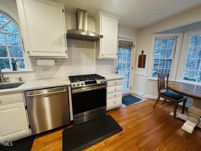 kitchen featuring stainless steel appliances, wall chimney exhaust hood, light countertops, and a sink