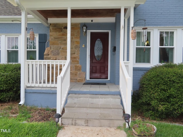 property entrance featuring covered porch, stone siding, and roof with shingles