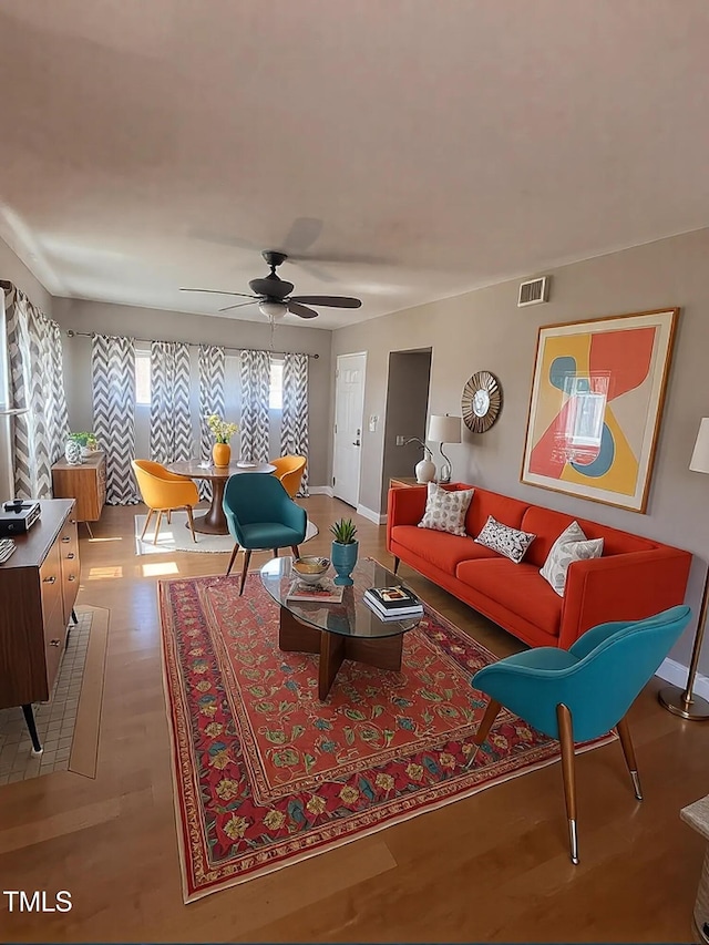 living room with baseboards, visible vents, wood finished floors, and a ceiling fan