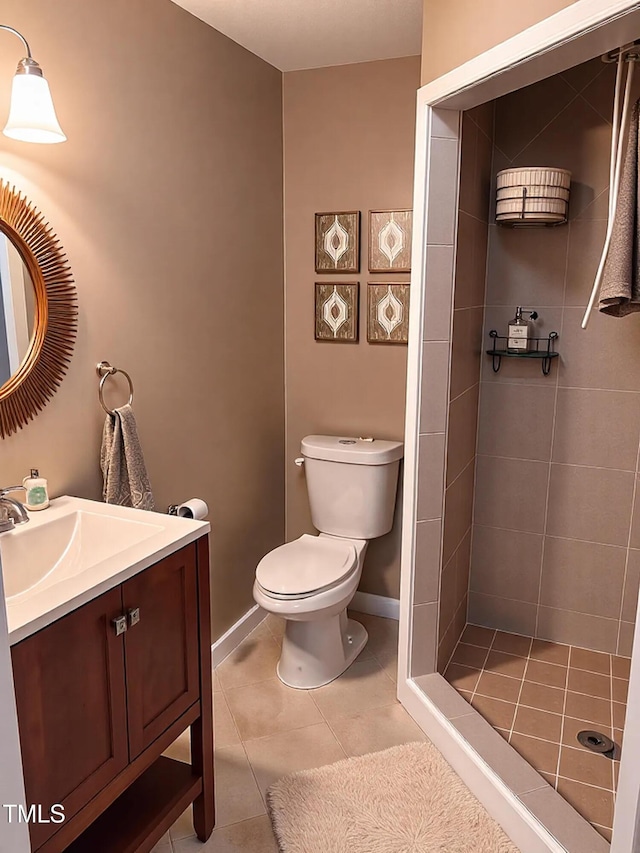 bathroom with vanity, toilet, baseboards, tile patterned floors, and tiled shower