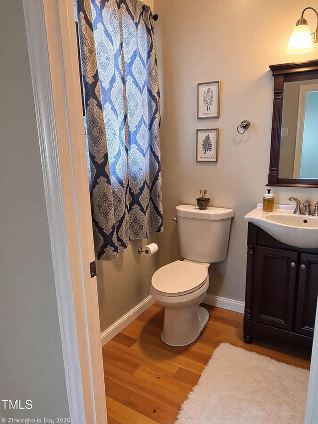 half bath with toilet, vanity, baseboards, and wood finished floors