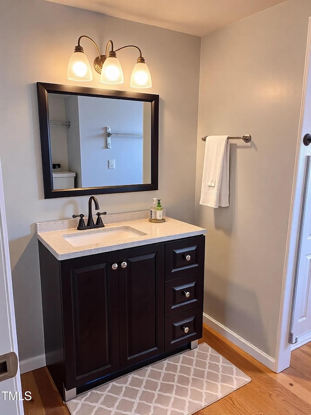 half bathroom with baseboards, toilet, wood finished floors, and vanity