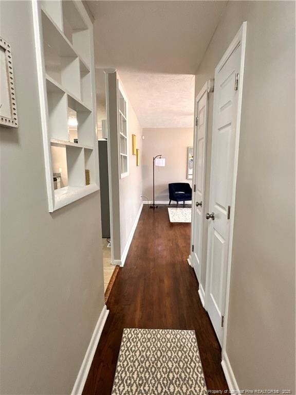 hall with dark wood-style floors, a textured ceiling, and baseboards