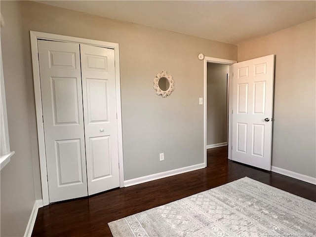 unfurnished bedroom featuring a closet, baseboards, and dark wood-style flooring