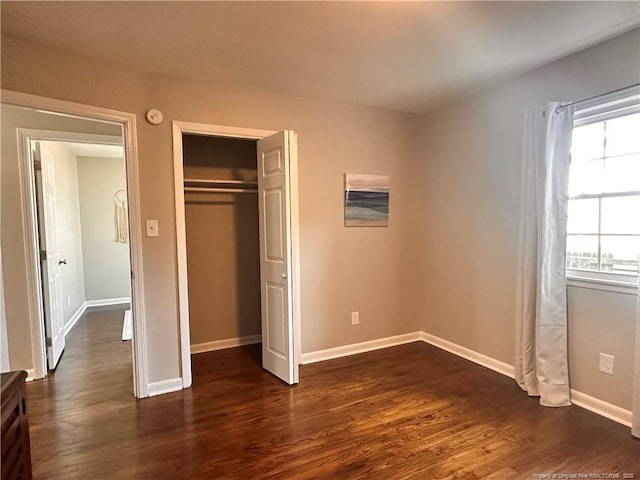 unfurnished bedroom with dark wood-style floors, a closet, and baseboards