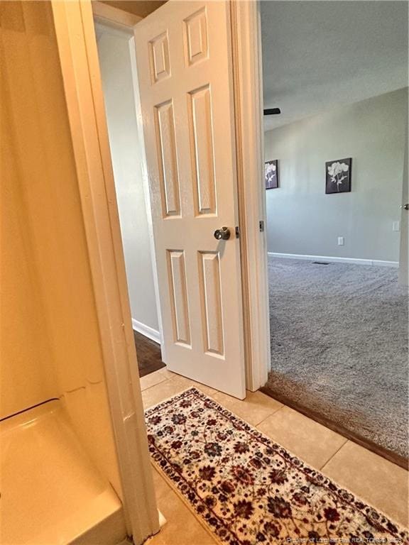 hallway with baseboards, carpet flooring, and tile patterned flooring