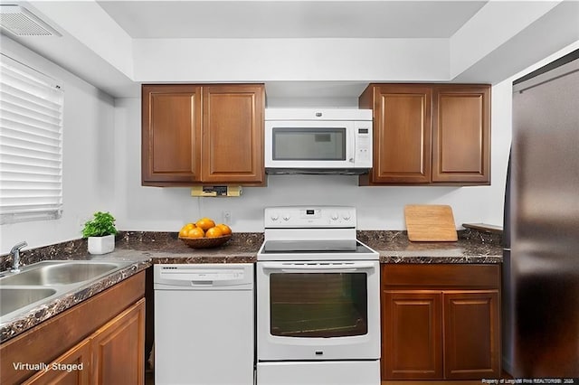 kitchen with a sink, visible vents, white appliances, and dark countertops