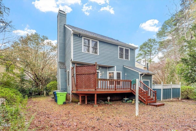 back of property with a chimney, a wooden deck, and fence