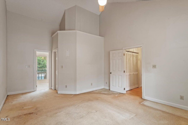 carpeted empty room with high vaulted ceiling and baseboards