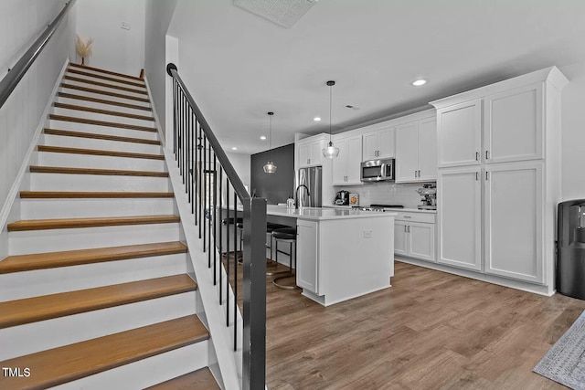 kitchen with a center island with sink, white cabinets, appliances with stainless steel finishes, and wood finished floors