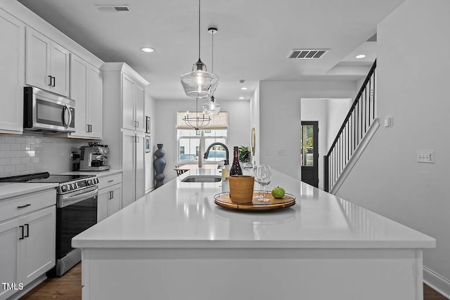 kitchen featuring visible vents, a kitchen island with sink, a sink, appliances with stainless steel finishes, and tasteful backsplash