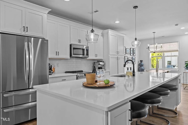 kitchen with a center island with sink, a sink, tasteful backsplash, wood finished floors, and appliances with stainless steel finishes