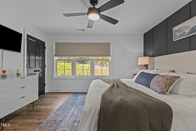 bedroom featuring a ceiling fan, wood finished floors, visible vents, and baseboards