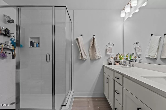 bathroom featuring double vanity, baseboards, a stall shower, and a sink