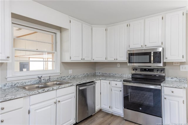 kitchen with stainless steel appliances, a sink, white cabinets, and light wood finished floors