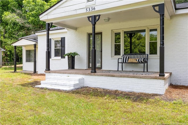 doorway to property with covered porch, brick siding, and a lawn