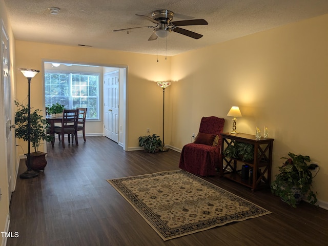 living area with a textured ceiling, ceiling fan, and dark wood-style flooring