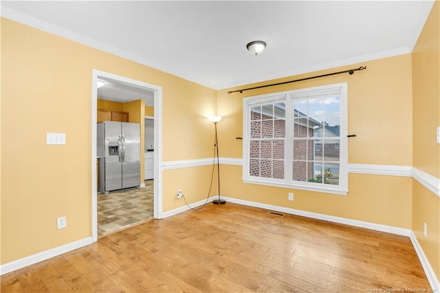 empty room featuring visible vents, baseboards, light wood-style flooring, and crown molding