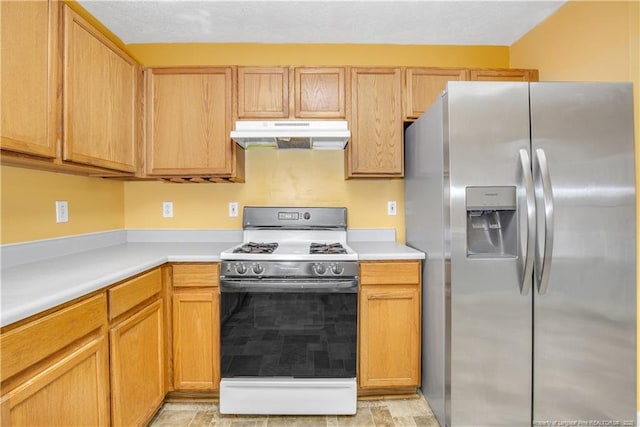 kitchen featuring under cabinet range hood, range with gas stovetop, stainless steel fridge, and light countertops