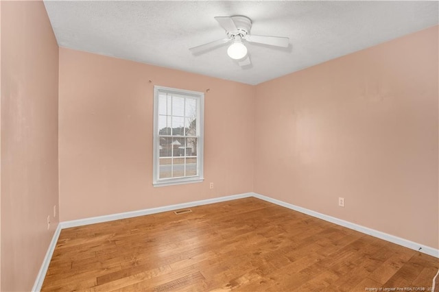 spare room featuring visible vents, a textured ceiling, light wood-style floors, baseboards, and ceiling fan