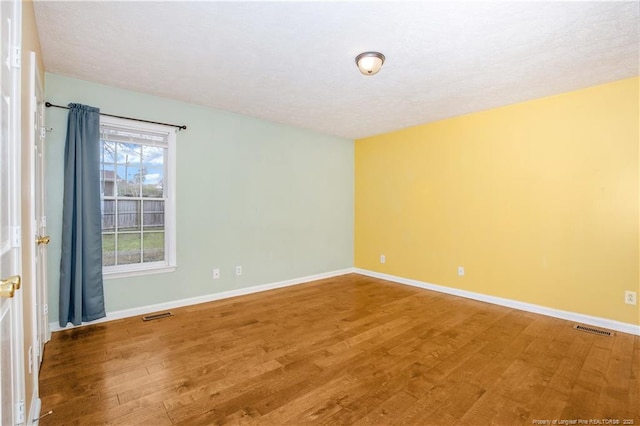 spare room with visible vents, baseboards, and wood finished floors