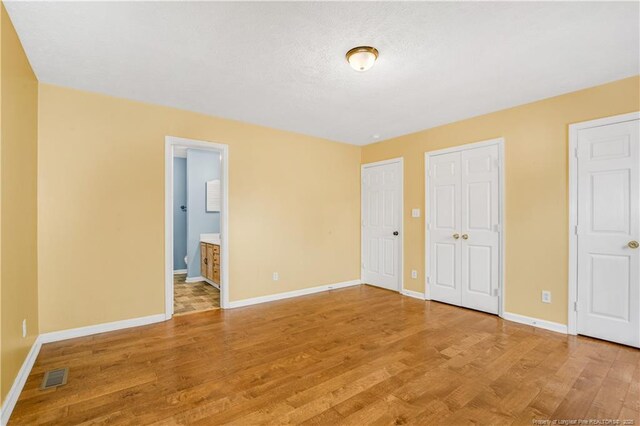 unfurnished bedroom with visible vents, multiple closets, ensuite bath, light wood-style floors, and baseboards