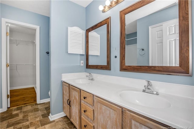 bathroom featuring double vanity, stone finish flooring, baseboards, and a sink