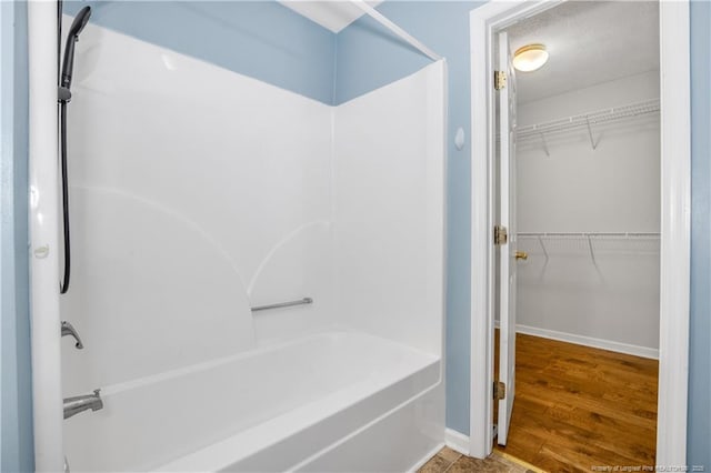 bathroom featuring shower / bathtub combination, a walk in closet, baseboards, and wood finished floors