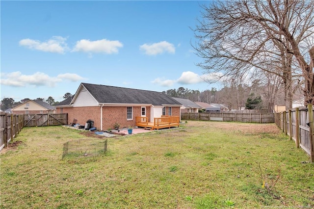 back of property with a deck, a fenced backyard, brick siding, and a lawn