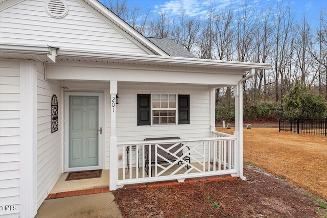 entrance to property with covered porch, a shingled roof, and fence
