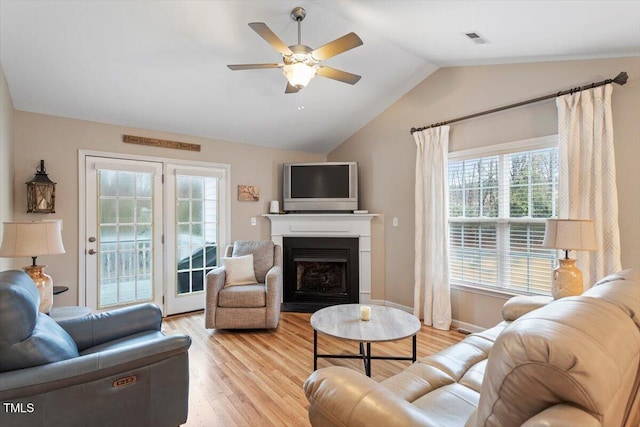 living area with visible vents, ceiling fan, vaulted ceiling, light wood-style flooring, and a fireplace