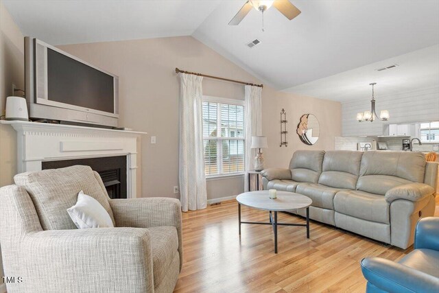 living area with lofted ceiling, ceiling fan with notable chandelier, visible vents, and light wood finished floors