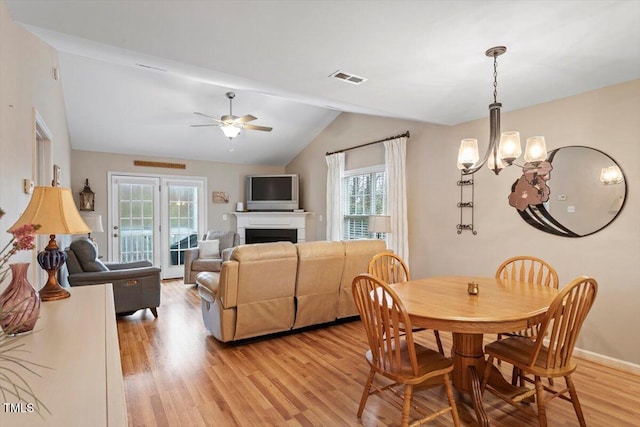 dining space with visible vents, lofted ceiling, ceiling fan with notable chandelier, a fireplace, and light wood-style floors