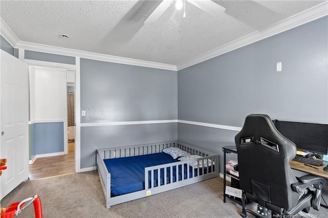 carpeted bedroom featuring a ceiling fan, baseboards, ornamental molding, a nursery area, and a textured ceiling