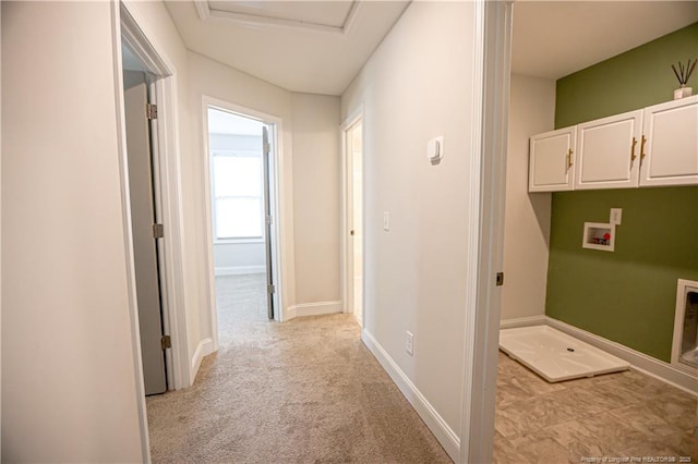 hallway featuring baseboards, attic access, and light carpet