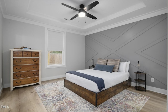 bedroom with light wood finished floors, crown molding, baseboards, a raised ceiling, and a ceiling fan