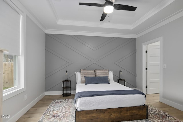 bedroom with a raised ceiling, ornamental molding, a ceiling fan, light wood finished floors, and baseboards